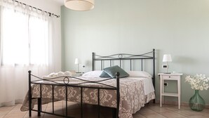 Un dormitorio con estructura de cama metálica, una mesita de noche con lámpara, una mesita auxiliar y un florero con flores.