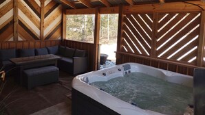 A wooden cabin with a hot tub, seating area, and large windows.