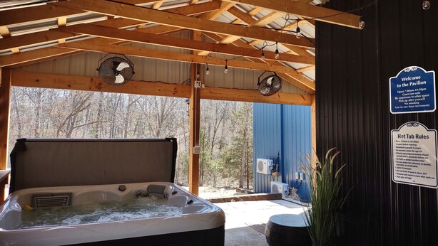 A hot tub under a wooden roof with fans, surrounded by a blue wall and a sign with rules.