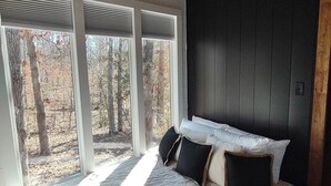 A bedroom with a large bed, a dark wall, and a view of trees through the window.
