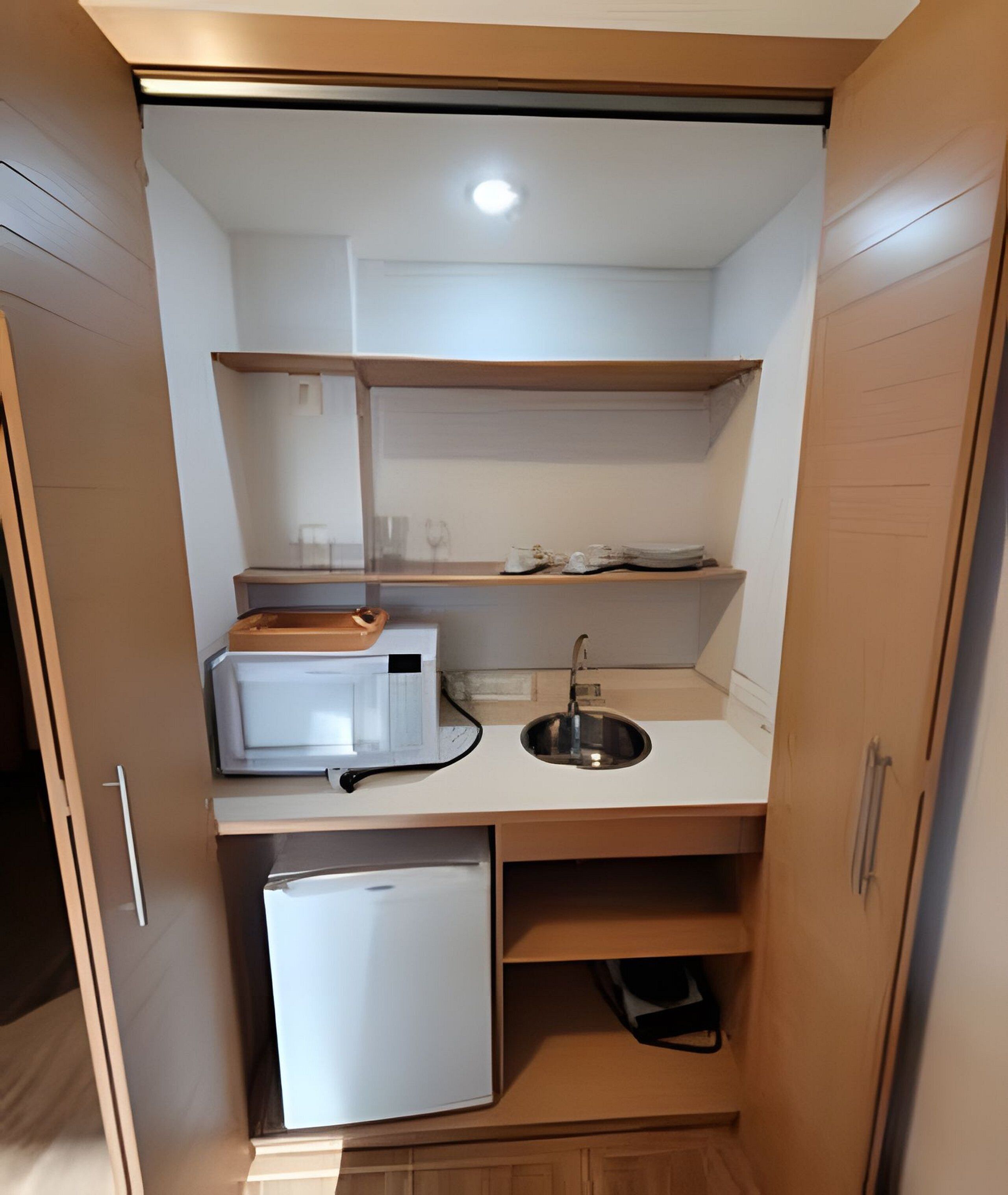 A compact kitchenette with a refrigerator, microwave, sink, and wooden shelves.