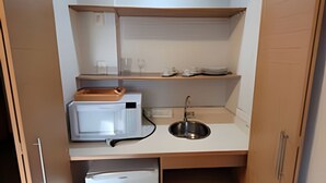 Une petite cuisine équipée comprenant un réfrigérateur, un four à micro-ondes, un évier et des étagères en bois.