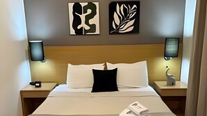 Une chambre d’hôtel avec un grand lit, deux tables de chevet, une tête de lit et des œuvres d’art accrochées au mur.