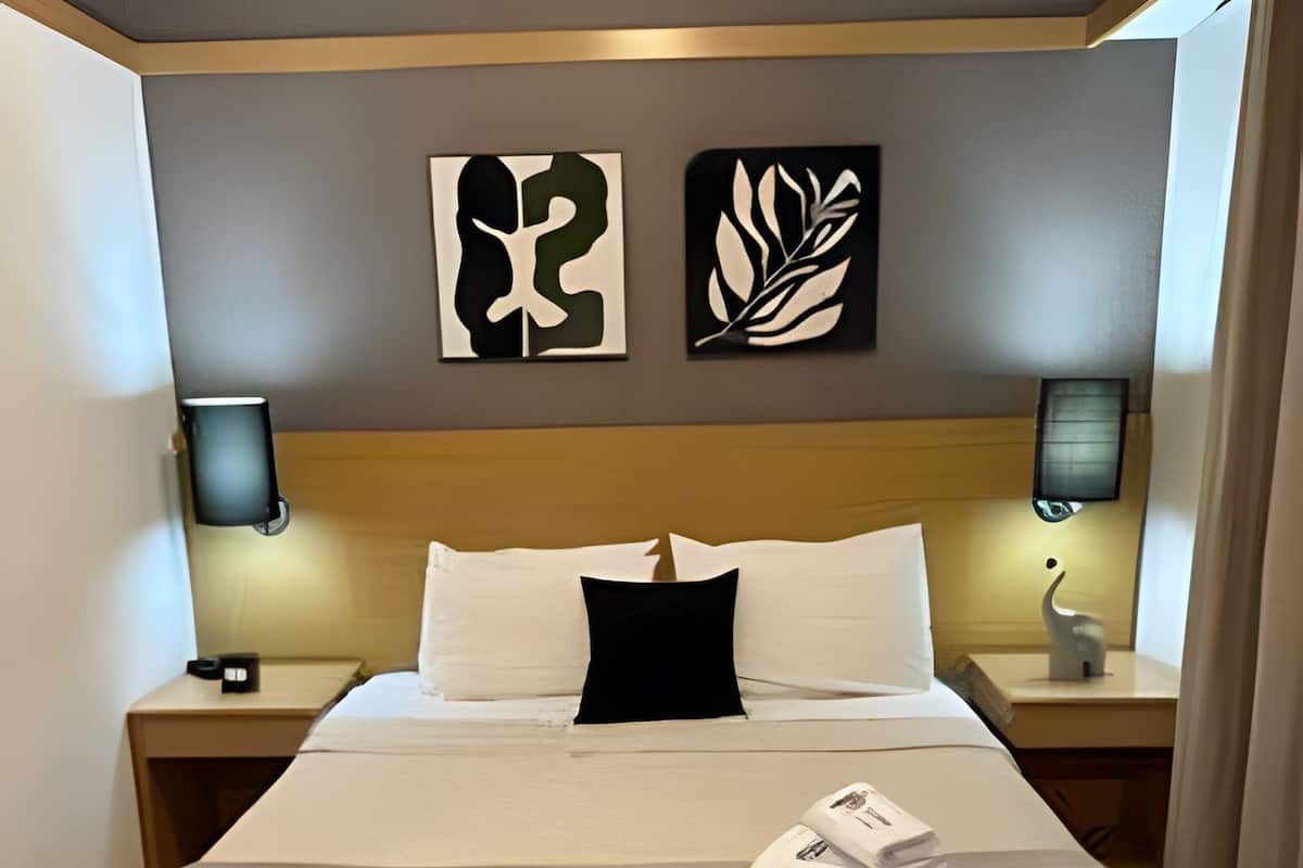 A hotel room with a large bed, two bedside tables, a headboard, and artwork on the wall.