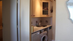 Cocina compacta con lavadora integrada, un lavamanos y un armario sobre la encimera.