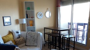 Una sala de estar con un sofá, una mesita, una estantería y un comedor con sillas.