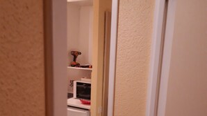 Un pasillo estrecho con un refrigerador blanco, un microondas y una pequeña área de cocina con un estante y un juguete.