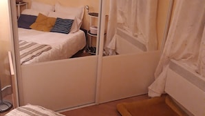 Un dormitorio con una cama, una mesita de noche, un espejo y una cortina.