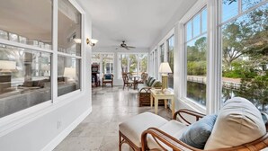 A sunlit room with large windows, wicker furniture, and a view of a body of water.
