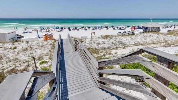 A beach with a wooden boardwalk leading to the shore, sandy beach, and beach umbrellas.