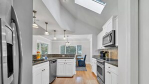 A modern kitchen with white cabinets, stainless steel appliances, and a skylight.