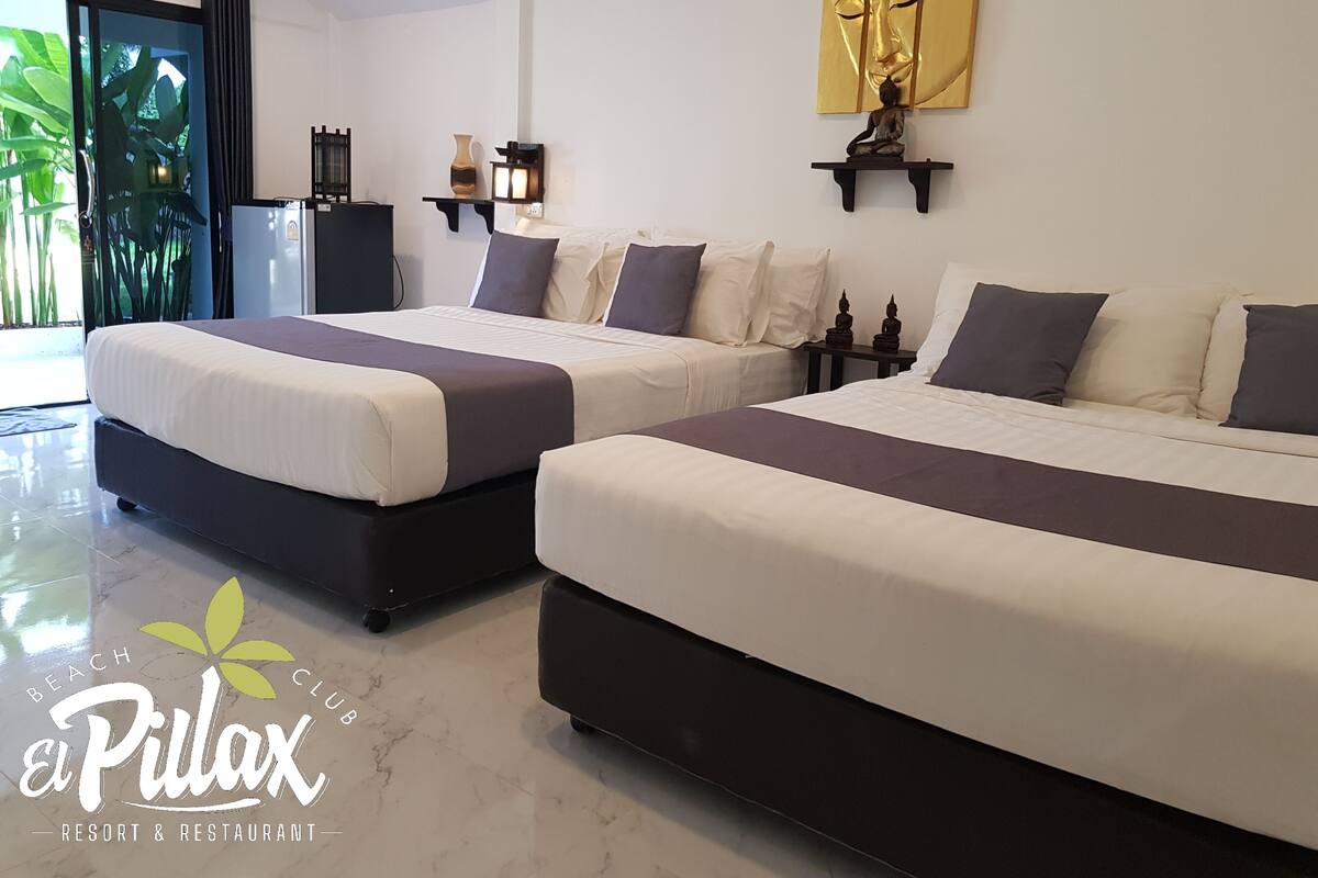 Habitación de hotel con dos camas, un ventanal con vistas a zonas verdes, una estatua de Buda montada en la pared y una obra de arte dorada decorativa.