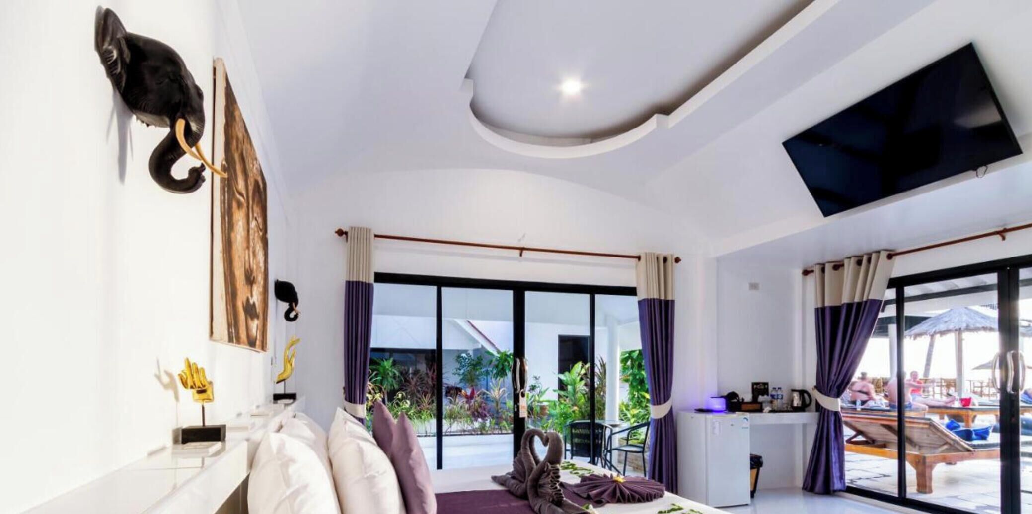 A modern hotel room with a sofa, a flat-screen TV, a dining area, and large windows.