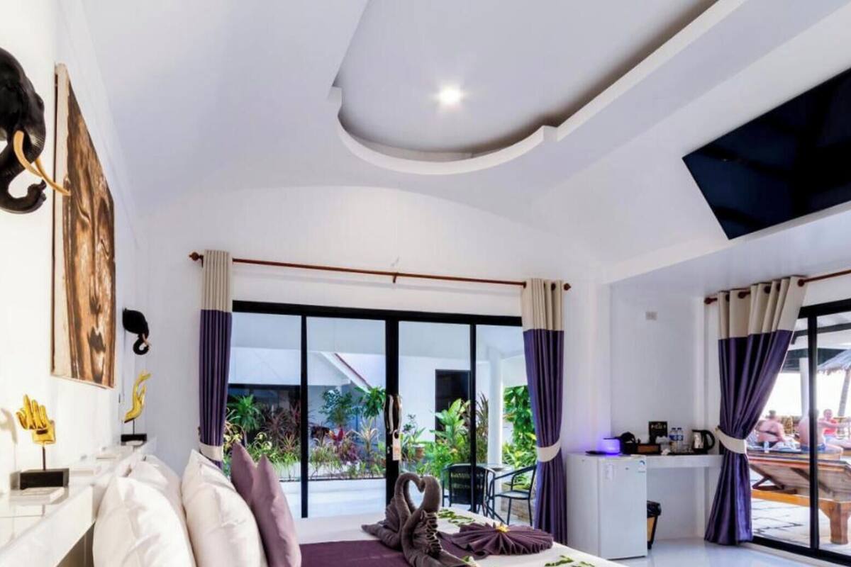 A modern hotel room with a sofa, a flat-screen TV, a dining area, and large windows.