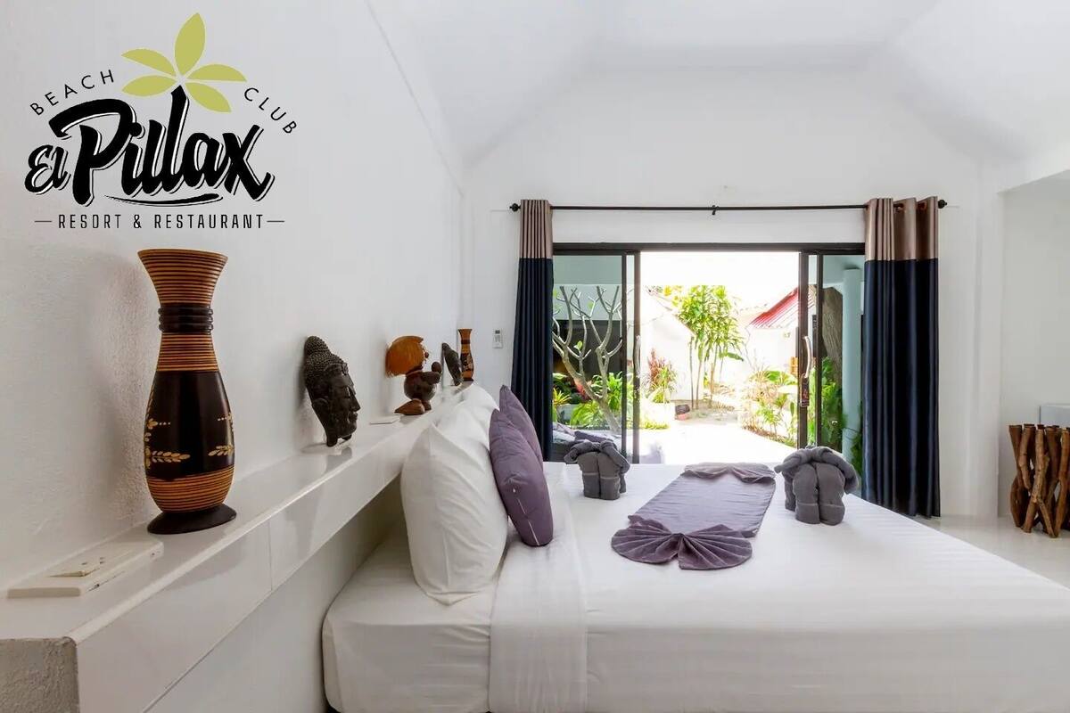 Un dormitorio con cama, almohadas, un florero y vistas al exterior.