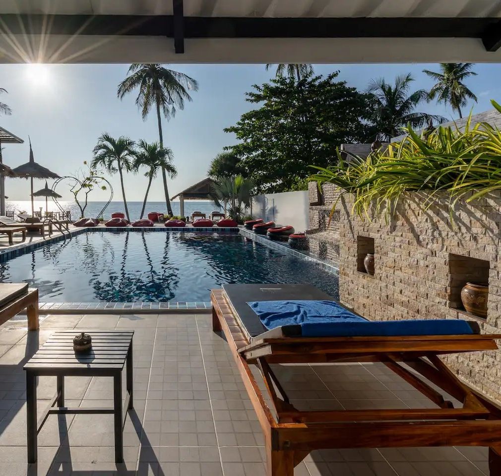 A poolside area with lounge chairs, a table, and a view of the ocean.