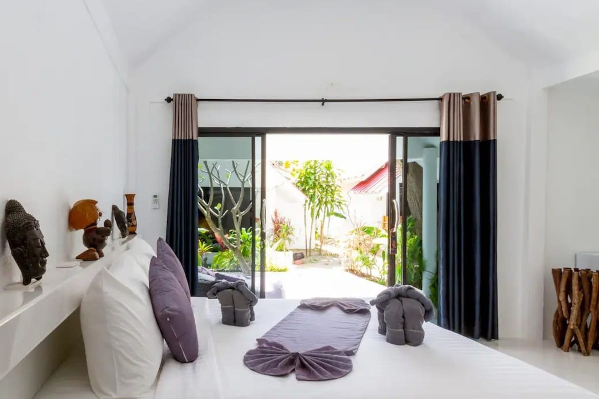 Un dormitorio con cama, almohadas, un florero y vistas al exterior.