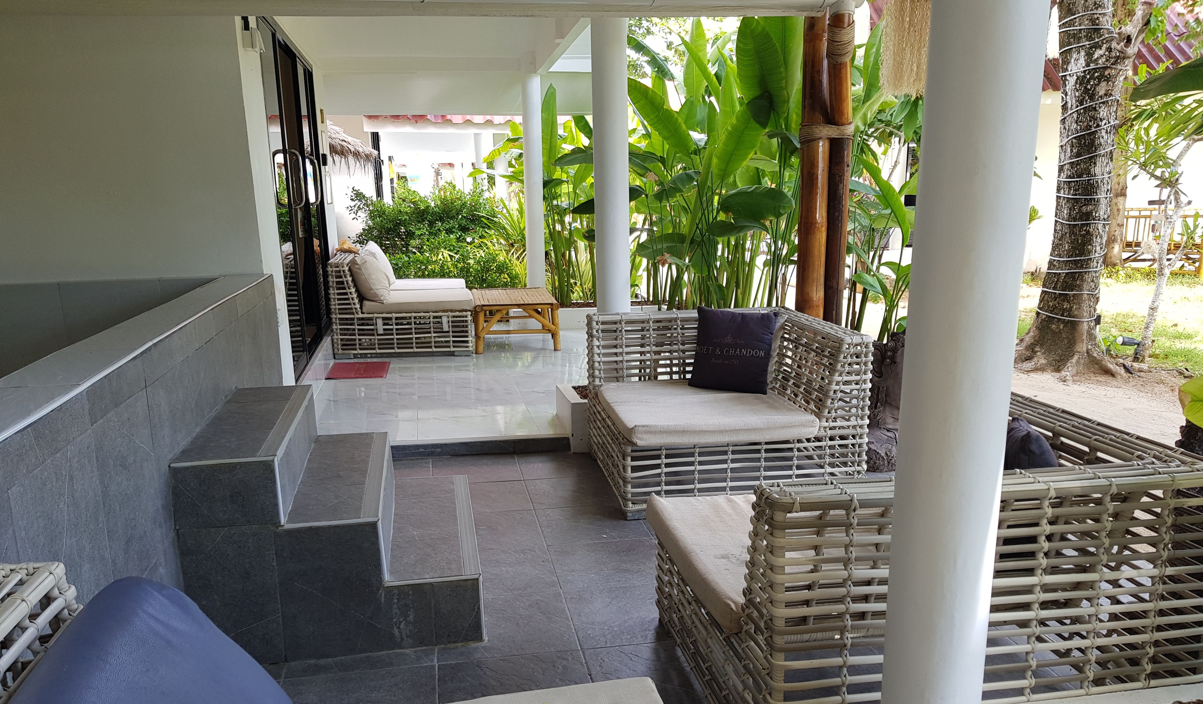 A covered outdoor seating area with wicker furniture and a stone-tiled floor.