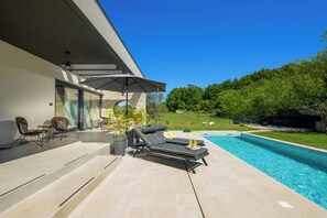Ein moderner Poolbereich im Freien mit Liegestuhl, Tisch und einer Topfpflanze.