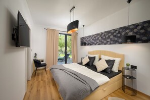 Ein modernes Schlafzimmer mit Bett, Fernseher, Nachttisch und Blick ins Freie.