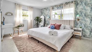 A bedroom with a bed, bedside tables, a desk, a chair, a ceiling fan, and a window with curtains.