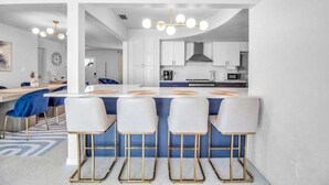 A modern kitchen with white cabinets, a central island with bar stools, and a chandelier.
