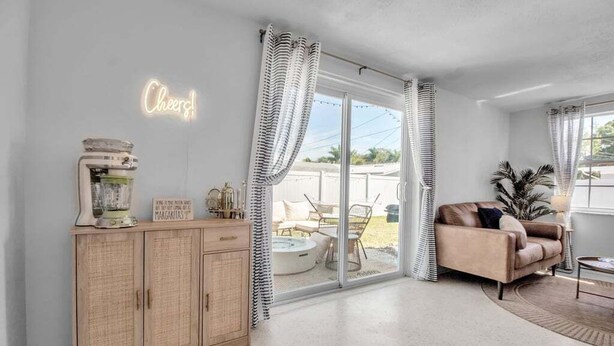 A spacious living room with a large sliding glass door leading to an outdoor patio, a wooden cabinet with a neon sign, and a comfortable beige sofa.