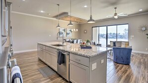 Une cuisine spacieuse dotée d’un grand îlot central, de luminaires suspendus et offrant une vue sur l’extérieur.