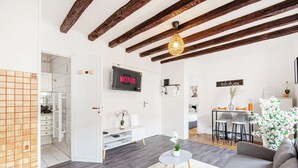 A modern living room with exposed wooden beams, a flat-screen TV, a dining area, and a small white table with a plant.