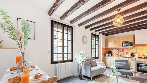 A modern kitchen with wooden beams, a dining area with a table set for breakfast, and a cozy seating area with a sofa and armchair.