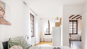 A bedroom with a bed, pillows, a bedside table, a lamp, a window, and a view of a bathroom.