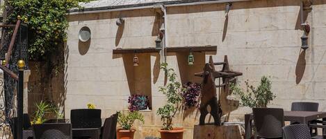 Un patio al aire libre con mobiliario de mimbre, un amplio toldo y una escultura de madera decorativa.