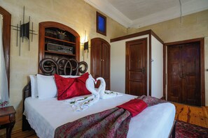 Quarto de hotel com cama, cabeceira de madeira, rádio fixado na parede e duas portas de madeira.