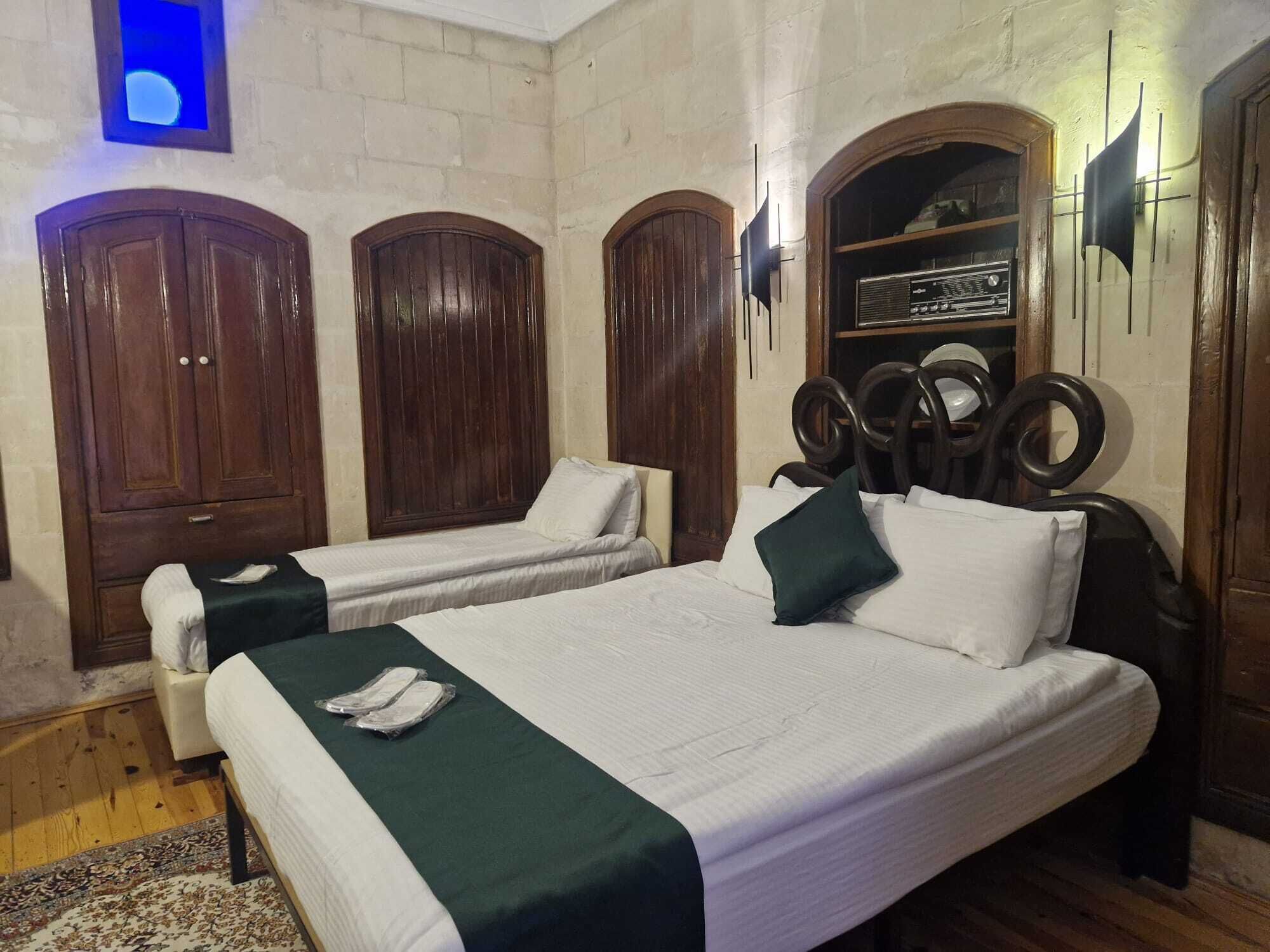 A room with two beds, wooden wardrobes, a radio, and a small blue-lit window.
