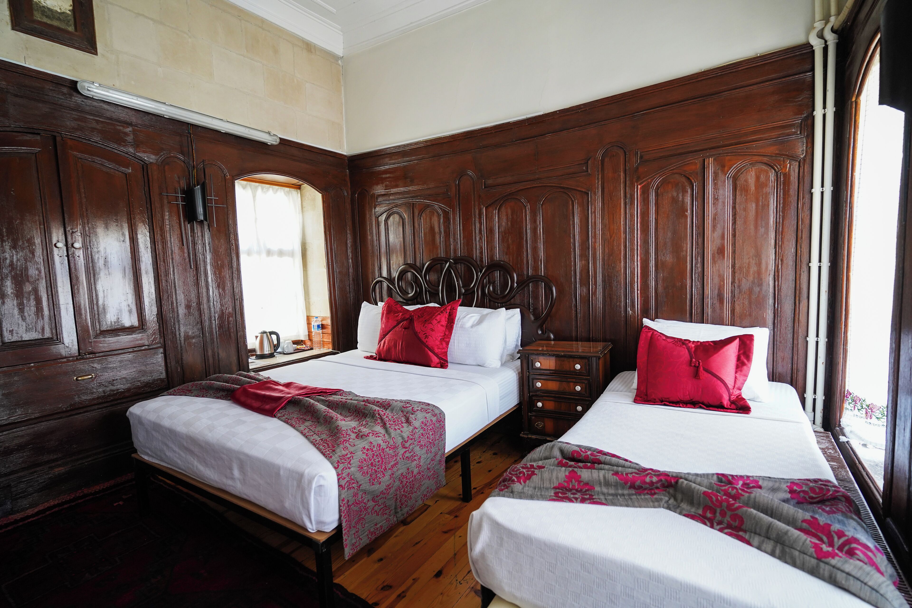 Habitación de hotel con dos camas, paneles de madera, una ventana con vistas y una mesita de noche con lámpara.