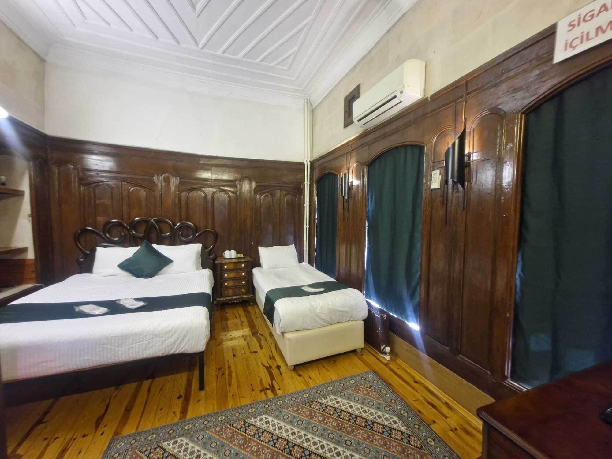 A hotel room with two beds, a wooden wardrobe, a small bedside table, and a patterned rug.