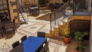 Un patio con zona de comedor, mobiliario exterior, plantas en macetas y una escalera que lleva a un nivel superior.