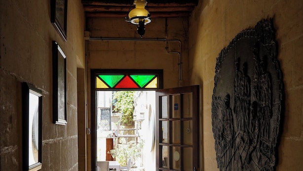Un pasillo con techo de madera, una puerta que da a un espacio exterior con planta en maceta y una escultura en la pared.