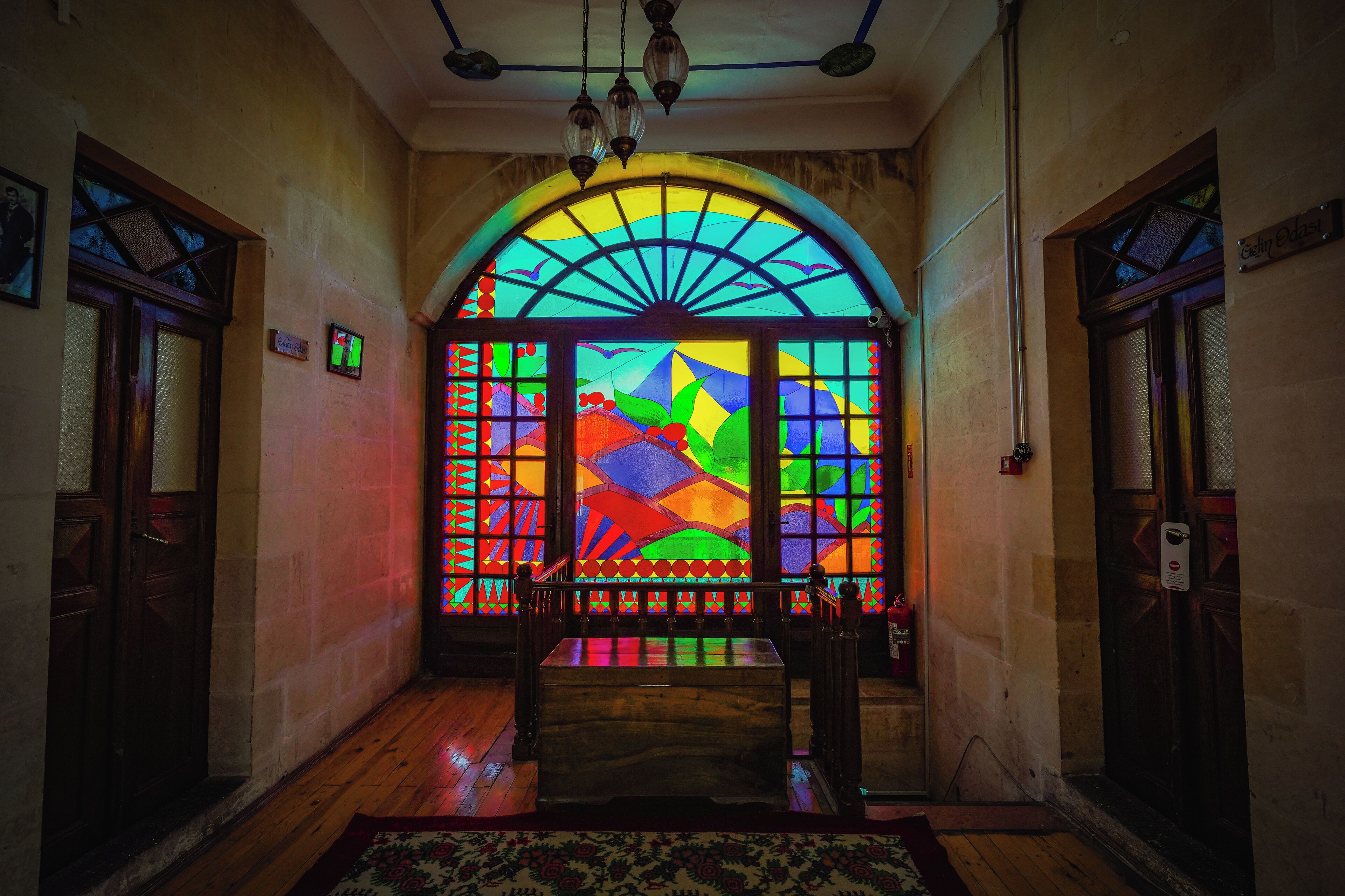 A hallway with a wooden bench, a patterned rug, and a stained glass window with colorful geometric patterns.