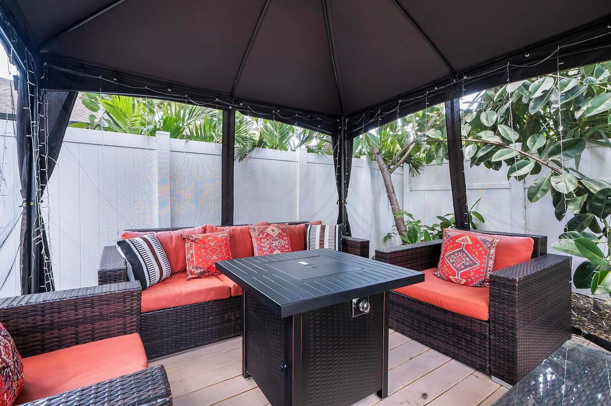 Une terrasse extérieure avec des meubles en osier, une table noire et des coussins rouges.