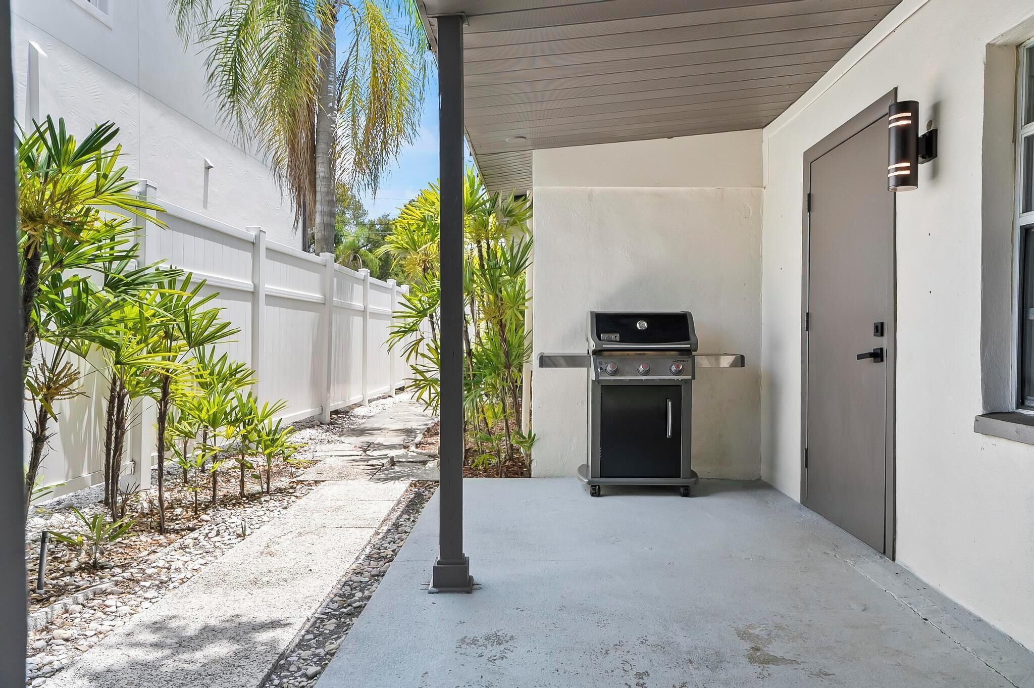 A covered outdoor area with a grill, a white fence, and small plants.