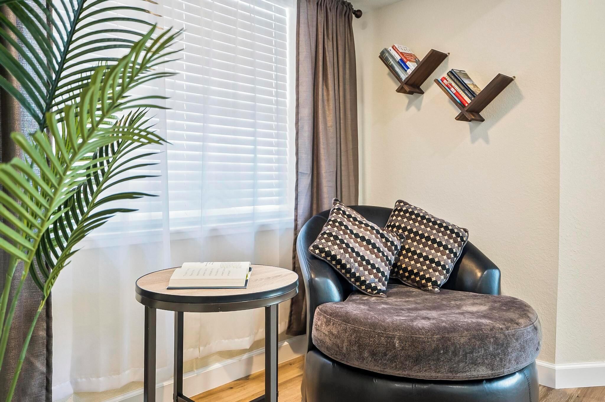 Una sala moderna con un sillón de cuero, una mesita redonda con un menú y una estantería llena de libros.