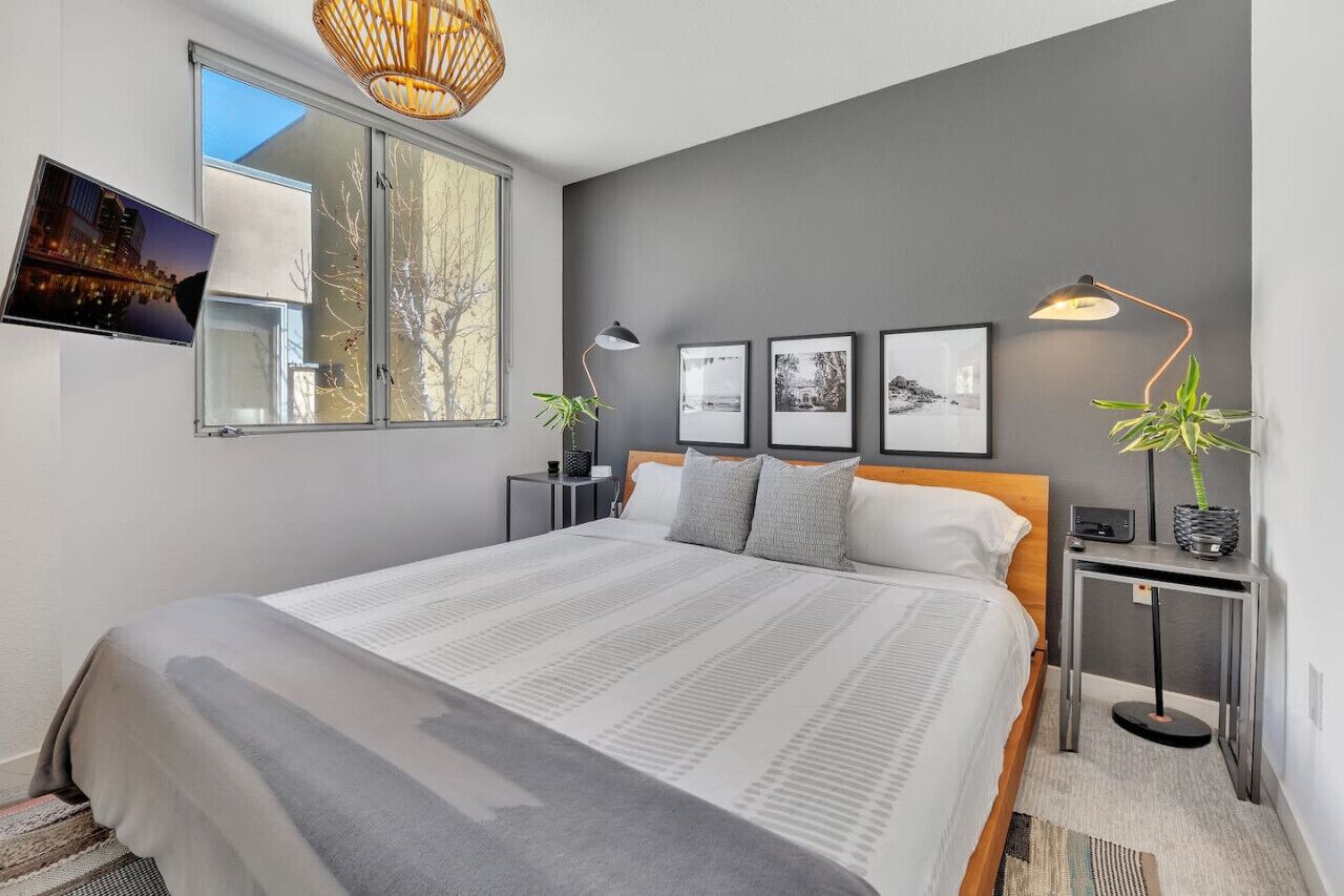 A modern bedroom with a large bed, a TV mounted on the wall, and framed pictures above the bed.