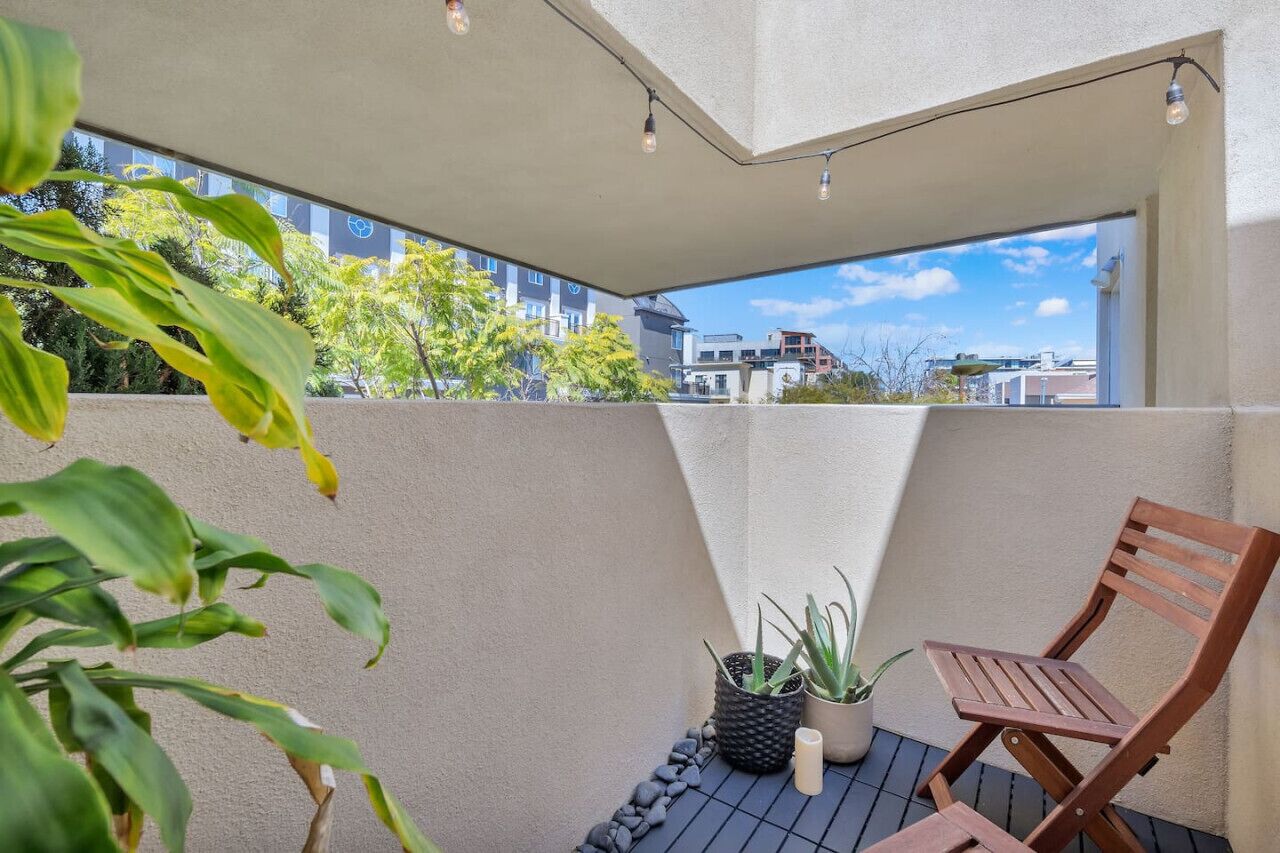 A balcony with a wooden chair, potted plants, and a view of buildings.