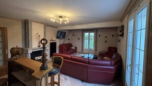 A living room with a fireplace, a red leather sofa, a dining table with chairs, and a television mounted on the wall.
