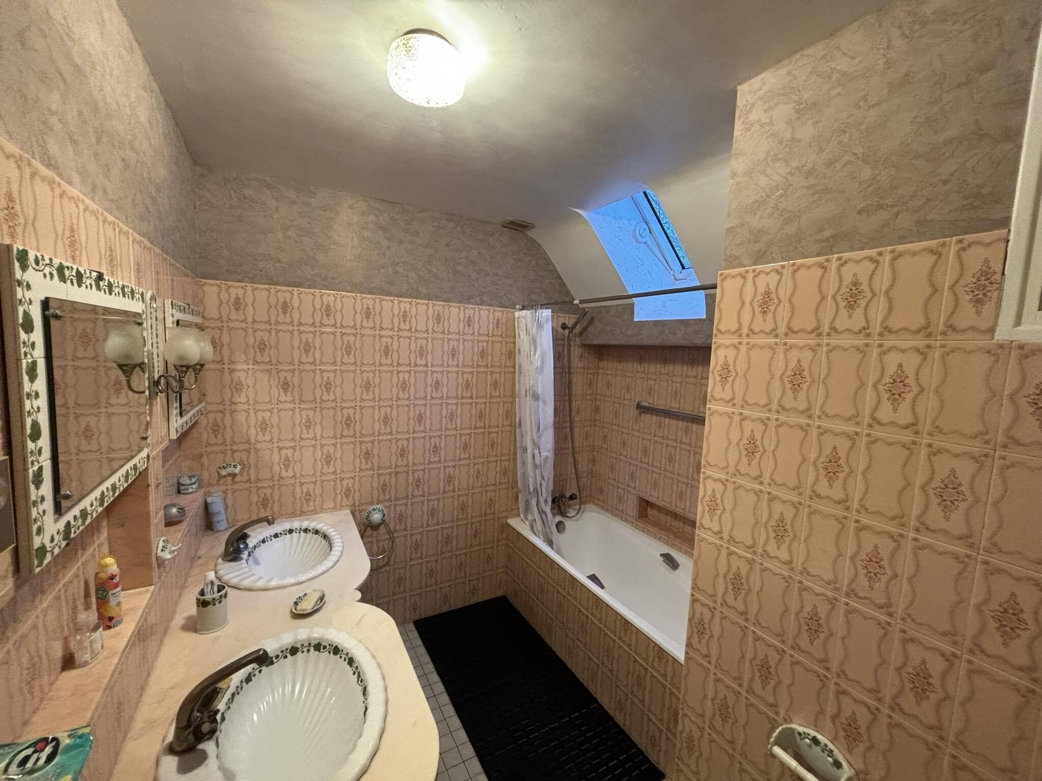 Een badkamer met twee wasbakken, een bad en een douche. Er is een dakraam boven de douche.