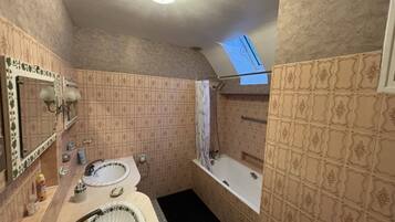 Een badkamer met twee wasbakken, een bad en een douche. Er is een dakraam boven de douche.