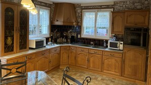 A kitchen with wooden cabinets, a stone wall, a built-in oven, and a window with lace curtains.