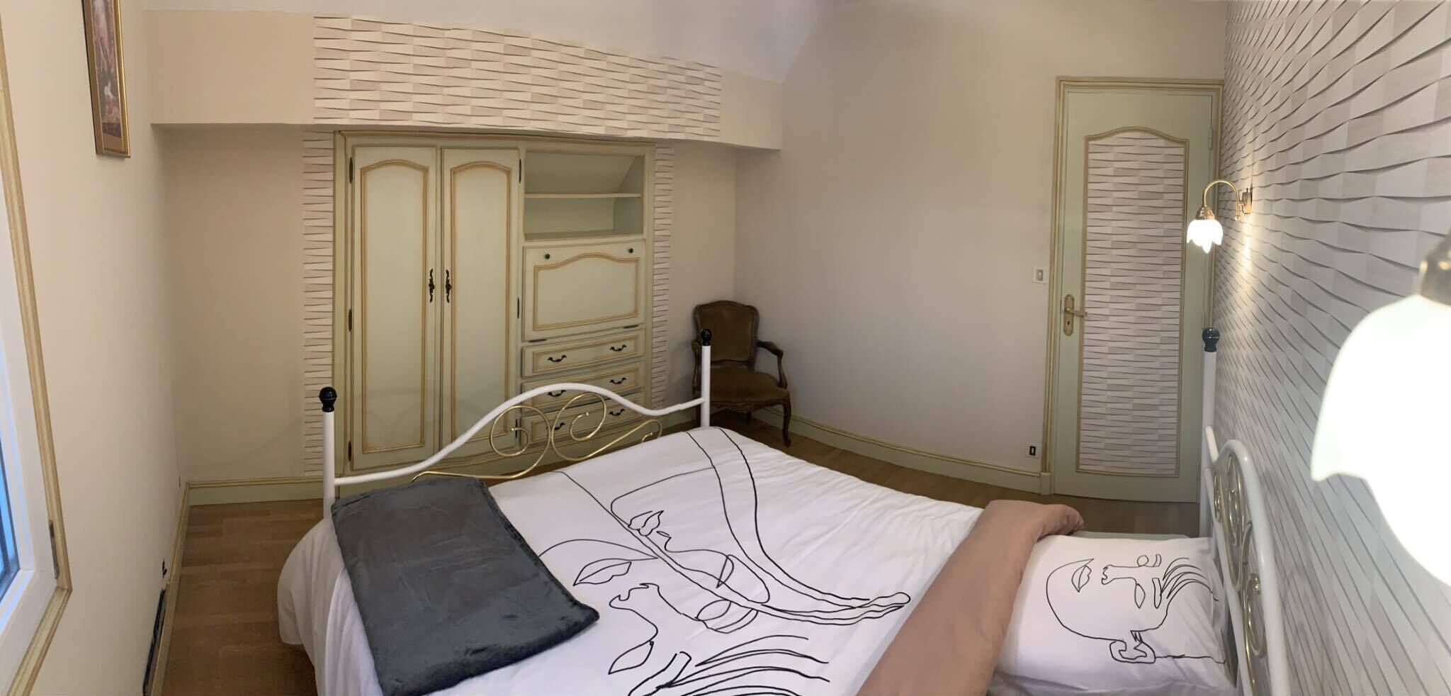 A bedroom with a bed, a chair, a wardrobe, and a door.
