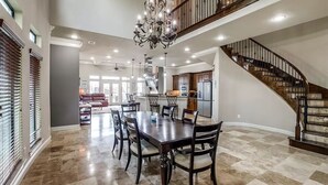 A spacious dining area with a large table and chairs, a chandelier, and a kitchen in the background. - Lakefront with dock, close to April Sound Country Club. BBQ Grill, Laundry (Montgomery)